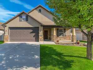 Craftsman house with board and batten siding, a front lawn, a porch, concrete driveway, and stone siding