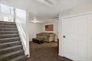 Living room featuring stairs, dark carpet, and a textured ceiling