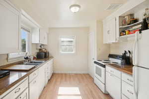Kitchen featuring white appliances, white cabinets, light wood finished floors, and dark countertops
