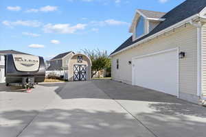 View of property exterior featuring roof with shingles, a garage, concrete driveway, and a storage unit