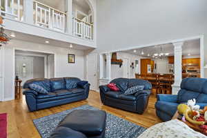 Living room with decorative columns, wood finished floors, recessed lighting, a chandelier, and a towering ceiling