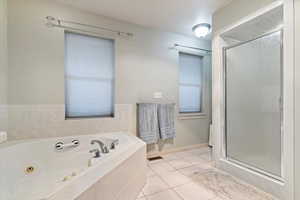 Full bath featuring light tile patterned floors, a tub with jets, and a shower stall