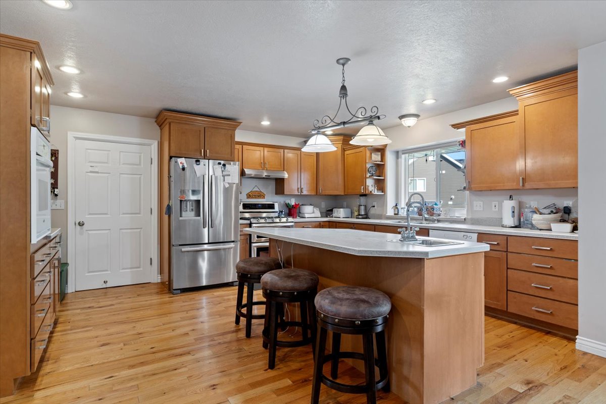 Kitchen with appliances with stainless steel finishes, light countertops, pendant lighting, brown cabinetry, and a kitchen island