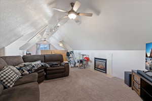 Carpeted living room with lofted ceiling, ceiling fan, rail lighting, a textured ceiling, and a high end fireplace