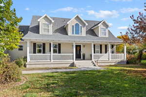 Cape cod-style house with a porch, a shingled roof, and a front yard