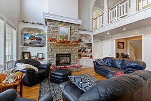 Living area with light wood-style floors, a stone fireplace, a high ceiling, and stairs