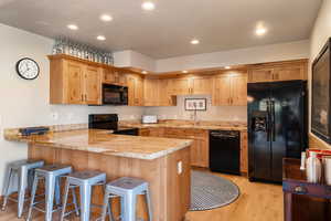Kitchen with black appliances, light wood-type flooring, a peninsula, recessed lighting, and a kitchen breakfast bar