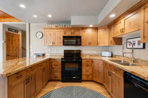 Kitchen with black appliances, light stone countertops, light wood finished floors, recessed lighting, and a peninsula