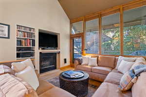Tiled living room with a glass covered fireplace, high vaulted ceiling, and built in shelves