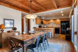 Dining area with light wood-style floors, a wooden ceiling with exposed beams, and recessed lighting