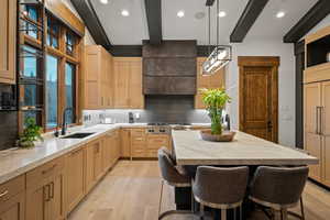 Kitchen featuring beamed ceiling, a breakfast bar, tasteful backsplash, light wood-type flooring, and hanging light fixtures