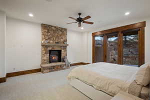 Carpeted bedroom with access to outside, a stone fireplace, a ceiling fan, and recessed lighting