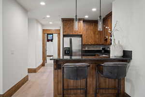 Kitchen featuring a kitchen breakfast bar, dark stone counters, stainless steel fridge, decorative backsplash, and wood finish cabinetry