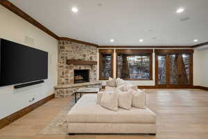 Living area with light wood-style floors, crown molding, a stone fireplace, and recessed lighting