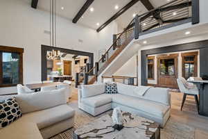Living area featuring a high ceiling, beam ceiling, wood finished floors, stairs, and a chandelier