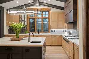 Kitchen featuring decorative backsplash, vaulted ceiling with beams, light wood-style floors, stainless steel gas cooktop, and light wood finish cabinetry