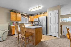 Kitchen featuring light carpet, light countertops, appliances with stainless steel finishes, a kitchen breakfast bar, and a textured ceiling