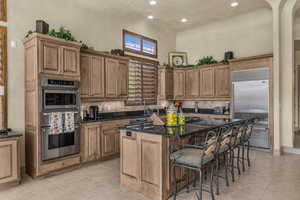 Kitchen featuring a breakfast bar, dark stone counters, stainless steel appliances, a kitchen island, and a high ceiling