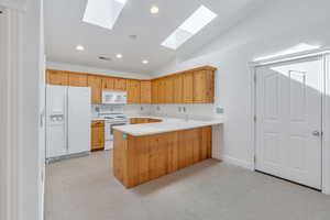 Kitchen featuring lofted ceiling, white appliances, light countertops, light colored carpet, and a peninsula