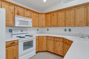 Kitchen featuring white appliances, light countertops, vaulted ceiling, recessed lighting, and light brown cabinets