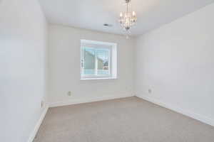 Carpeted empty room featuring baseboards and a chandelier