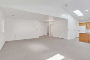 Unfurnished living room with light carpet, a skylight, a chandelier, recessed lighting, and high vaulted ceiling