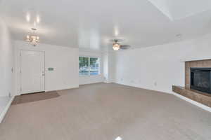 Unfurnished living room with a fireplace, carpet flooring, a chandelier, and ceiling fan