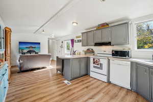 Kitchen featuring gray cabinetry, a peninsula, white appliances, open floor plan, and light wood-style flooring