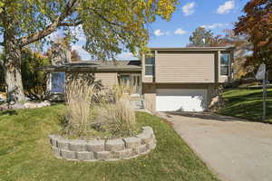 Tri-level home featuring brick siding, a front yard, an attached garage, a chimney, and concrete driveway