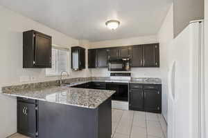 Kitchen featuring white appliances, light stone counters, a peninsula, and light tile patterned floors