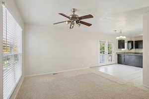 Unfurnished living room featuring a ceiling fan, light carpet, a chandelier, light tile patterned floors, and french doors