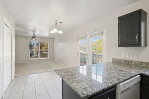 Kitchen with dark cabinetry, light colored carpet, dishwasher, light tile patterned floors, and light stone countertops