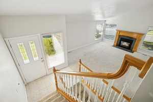 Entrance foyer with healthy amount of natural light, lofted ceiling, a fireplace, light tile patterned floors, and light colored carpet