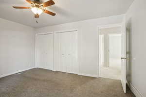 Unfurnished bedroom with multiple closets, dark colored carpet, a ceiling fan, and a baseboard radiator