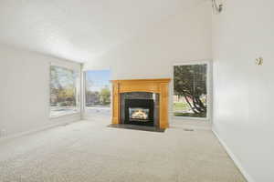 Unfurnished living room featuring carpet flooring, a fireplace, plenty of natural light, and high vaulted ceiling