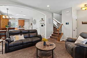 Carpeted living room with stairway, arched walkways, a chandelier, and recessed lighting