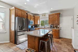 Kitchen featuring brown cabinets, appliances with stainless steel finishes, backsplash, light stone countertops, and recessed lighting