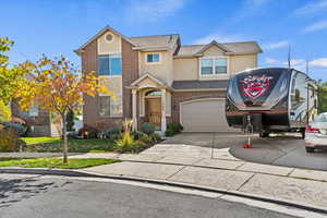 Traditional-style house with stucco siding, driveway, brick siding, a shingled roof, and a garage