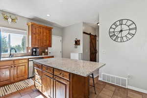 Kitchen with brown cabinets, light stone countertops, a kitchen island, dark tile patterned flooring, and dishwasher