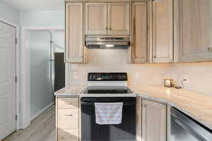 Kitchen featuring black range with electric stovetop, light countertops, light brown cabinetry, decorative backsplash, and under cabinet range hood