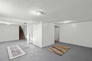 Finished basement featuring a textured ceiling and stairway
