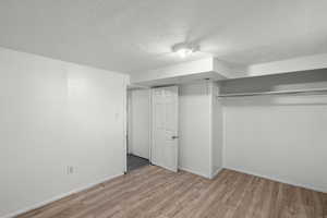 Unfurnished bedroom featuring a textured ceiling, light wood finished floors, and a closet