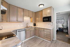 Kitchen featuring black appliances, light wood-style flooring, tasteful backsplash, under cabinet range hood, and light stone counters
