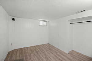 Below grade area with light wood-style floors and a textured ceiling
