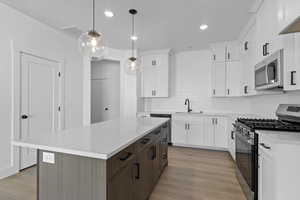 Kitchen with stainless steel appliances, hanging light fixtures, light stone countertops, white cabinets, and a center island