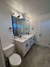 Full bathroom with double vanity, a textured ceiling, and dark tile patterned flooring