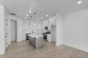 Kitchen with a kitchen island, appliances with stainless steel finishes, white cabinets, decorative light fixtures, and recessed lighting