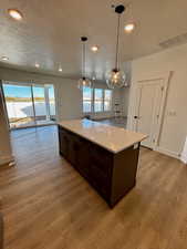 Kitchen with dark brown cabinets, decorative light fixtures, a textured ceiling, light stone countertops, and light wood-type flooring