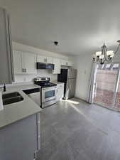 Kitchen featuring stainless steel appliances, a chandelier, white cabinetry, light stone countertops, and stone tile floors