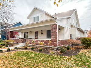 View of front of property featuring board and batten siding, covered porch, brick siding, and a front yard